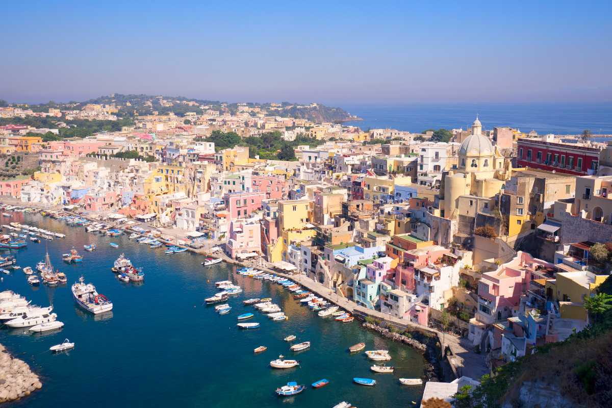 Scena vivace di street food a Procida: persone che gustano lingue di bue e frittura di pesce tra le vie colorate vicino al porto